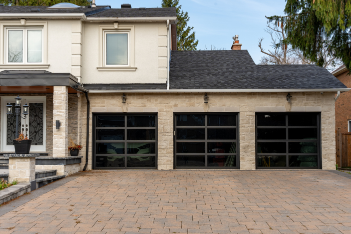 Front view of a stone garage with three black full view glass garage doors by Dodds.