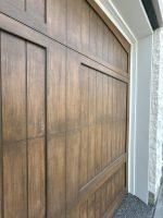 Straight-on front view of two matching custom steel wood overlay garage doors in white stone archways.