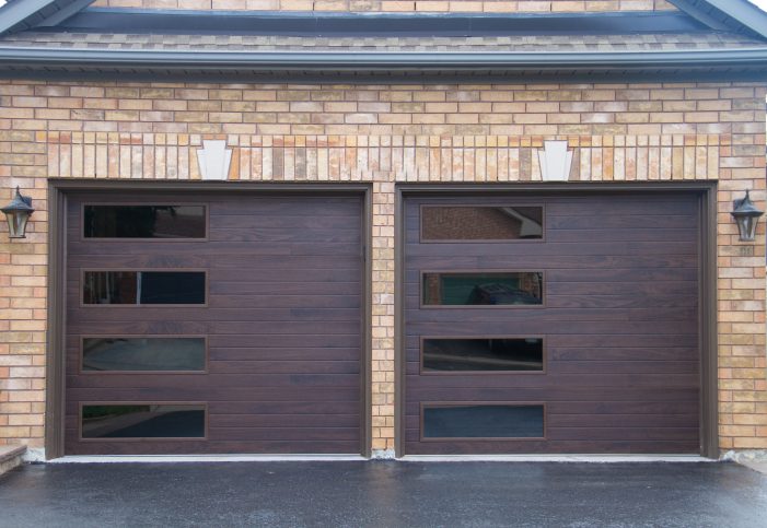 Symmetrical view of two dark walnut woodgrain plank-style garage doors with contemporary side-stacked tinted window panes