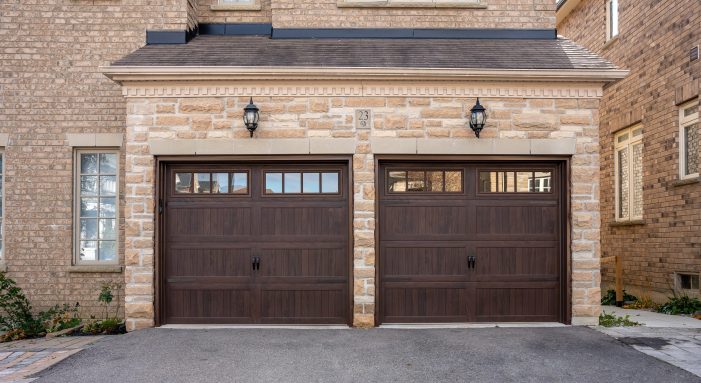 Two long panel coach house garage doors in Walnut Woodtones with top windows, installed on a stone-facade home in Richmond Hill, Ontario.