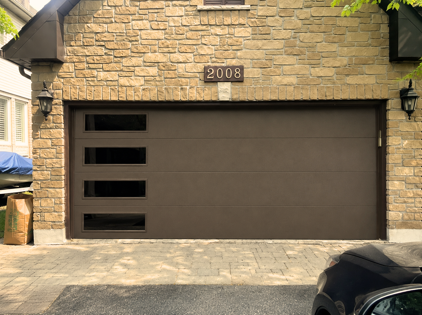 Modern dark brown flush garage door with vertical side windows installed on a stone-facade home by Dodds Garage Doors.