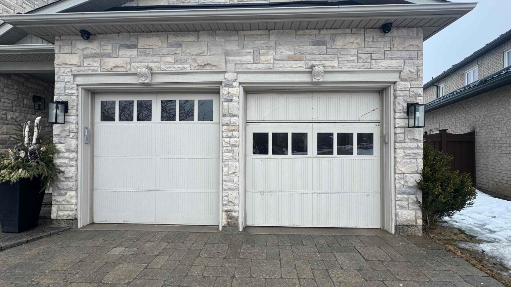 Old, worn white panel garage doors on a stone home before custom replacement in Woodbridge, Ontario.