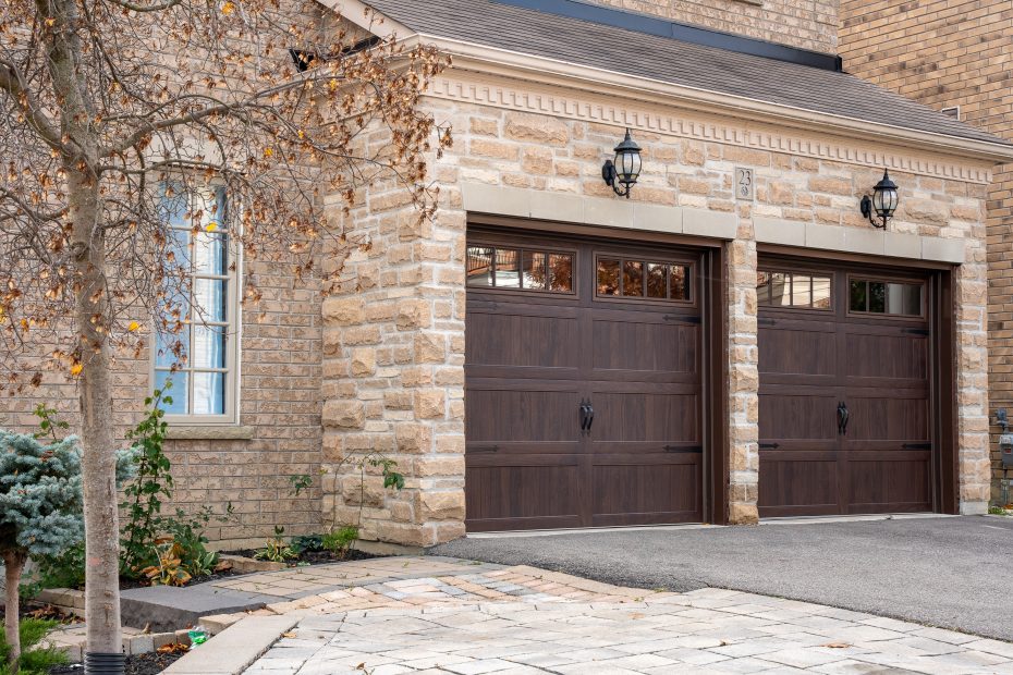 Side view of two long-panel walnut coach house garage doors accenting the textured stone masonry of a modern suburban home.