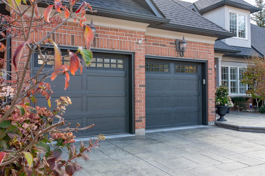 Side view of two dark iron ore recessed long panel garage doors installed on a brick house by Dodds.