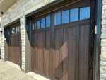 Upclose angle view showing dark wood-grain carriage house garage doors and arched windows installed in Woodbridge, Ontario.