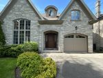 Front view of a stone home showcasing a dark wood entry door alongside a matching custom steel wood overlay garage door.