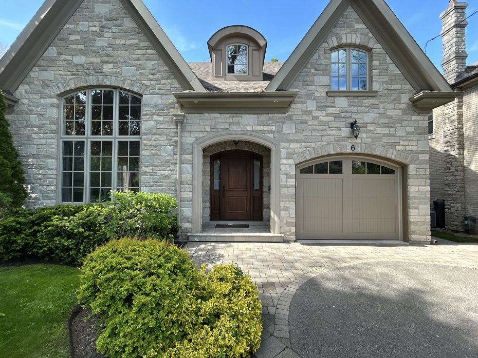 Front view of a stone home showcasing a dark wood entry door alongside a matching custom steel wood overlay garage door.