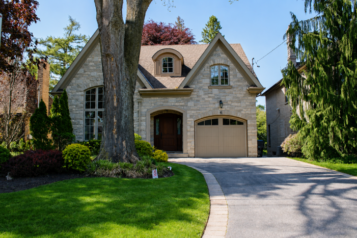 Full exterior view of a luxury stone house featuring a beige custom steel wood overlay carriage-style garage door and landscaped front yard.