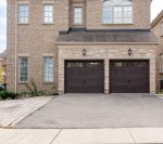 Clear straight-on shot of two traditional long-panel walnut woodtone garage doors on a brick residential home in Richmond Hill.
